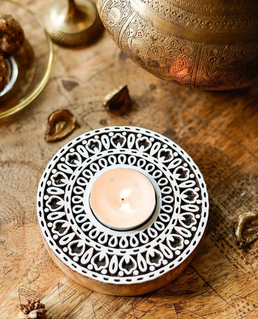 Decorative wooden tealight holder with a lit candle on a wooden surface