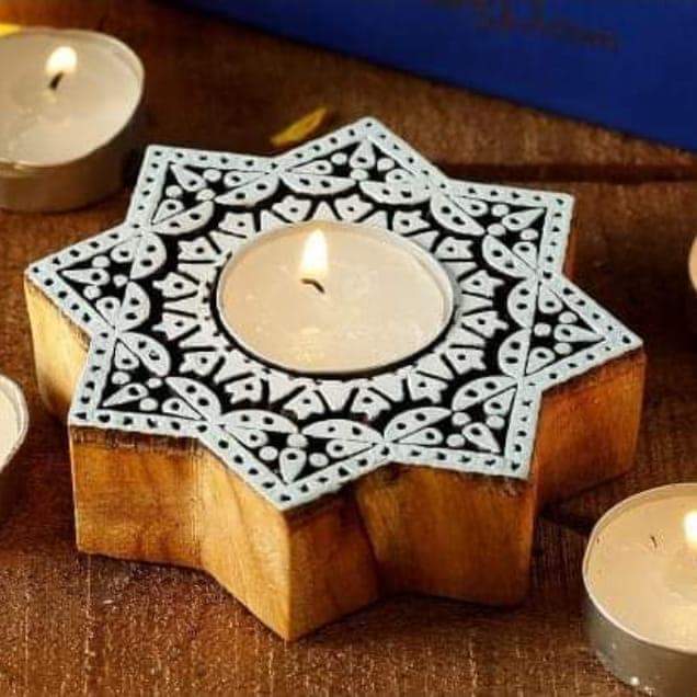 Decorative wooden candle holder with a star-shaped cutout holding a lit candle on a wooden surface.