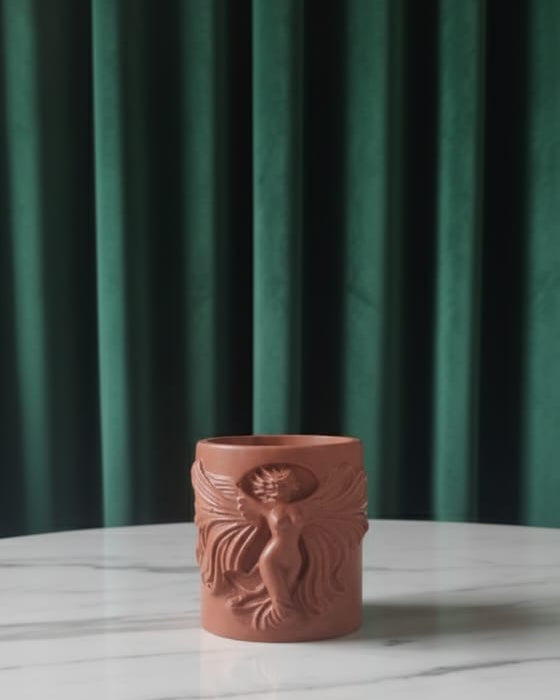 Jesmonite candle jar with a design on a marble table against a green curtain background