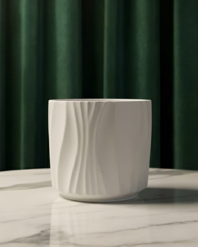 White ceramic candle jar with wavy texture on a marble surface with a green curtain background