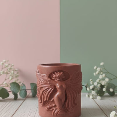 The Risen Phoenix Relief Jesmonite Candle, a terracotta-colored candle with a detailed phoenix design, displayed on a wooden surface.