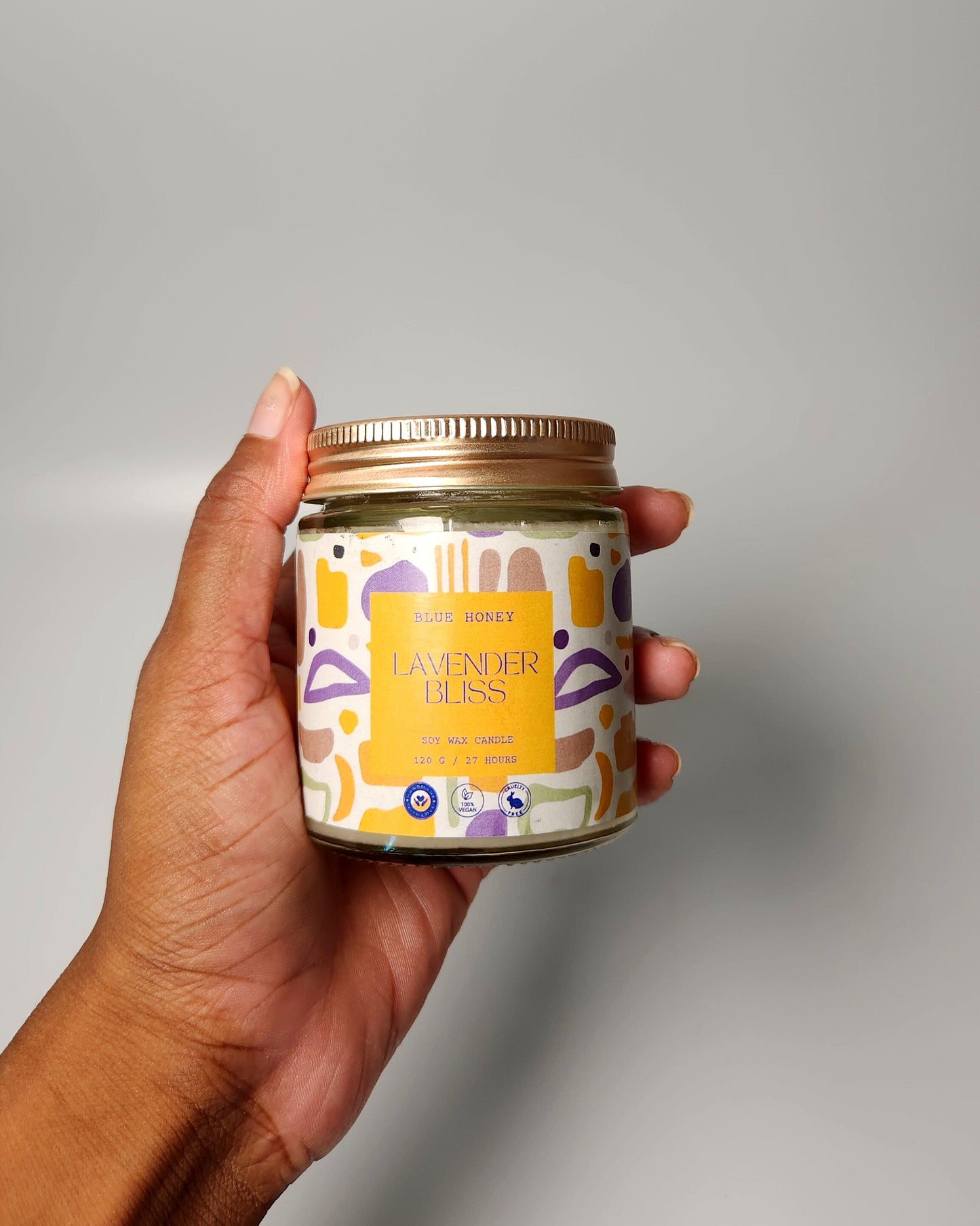 Hand holding a candle jar with a colorful label against a plain background