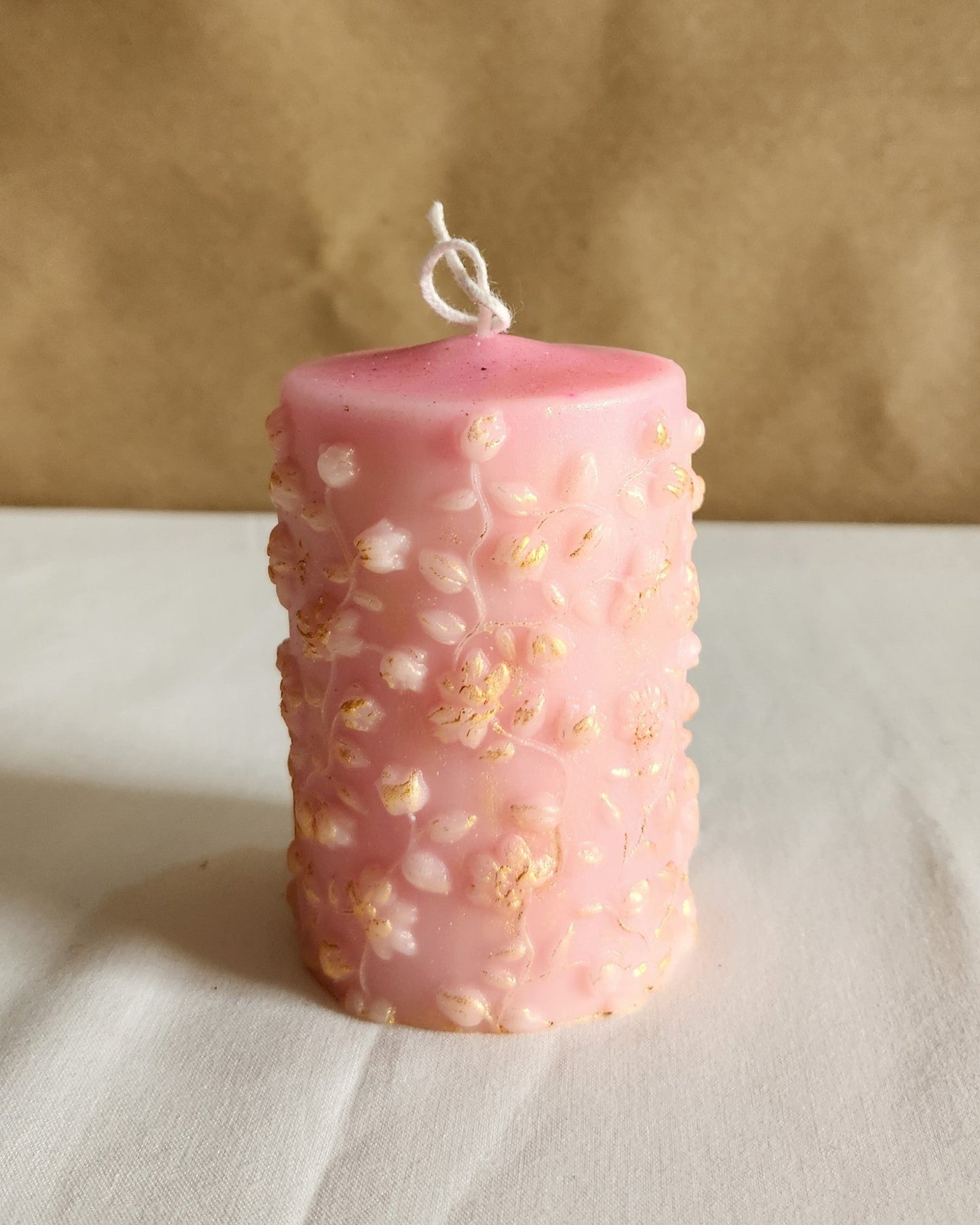 baby pink raat raani scented flower pillar candle gold dusted with cotton wick on a table top.