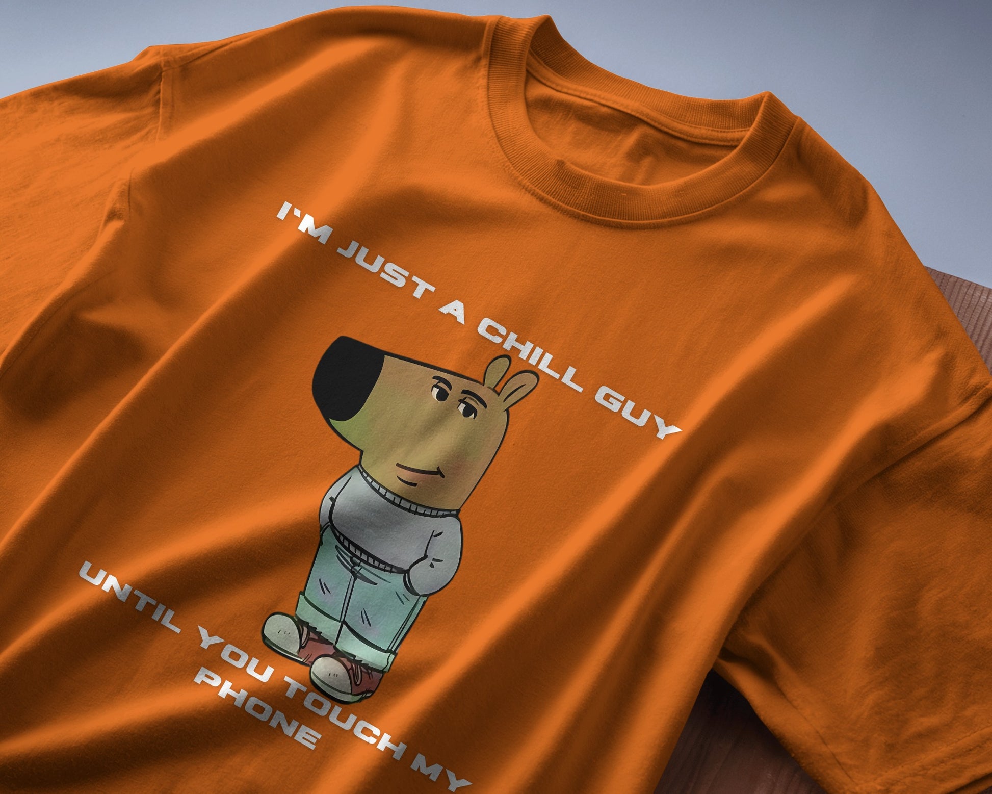 orange "I’m Just a Chill Guy… Until You Touch My Phone" tshirt laying on the table