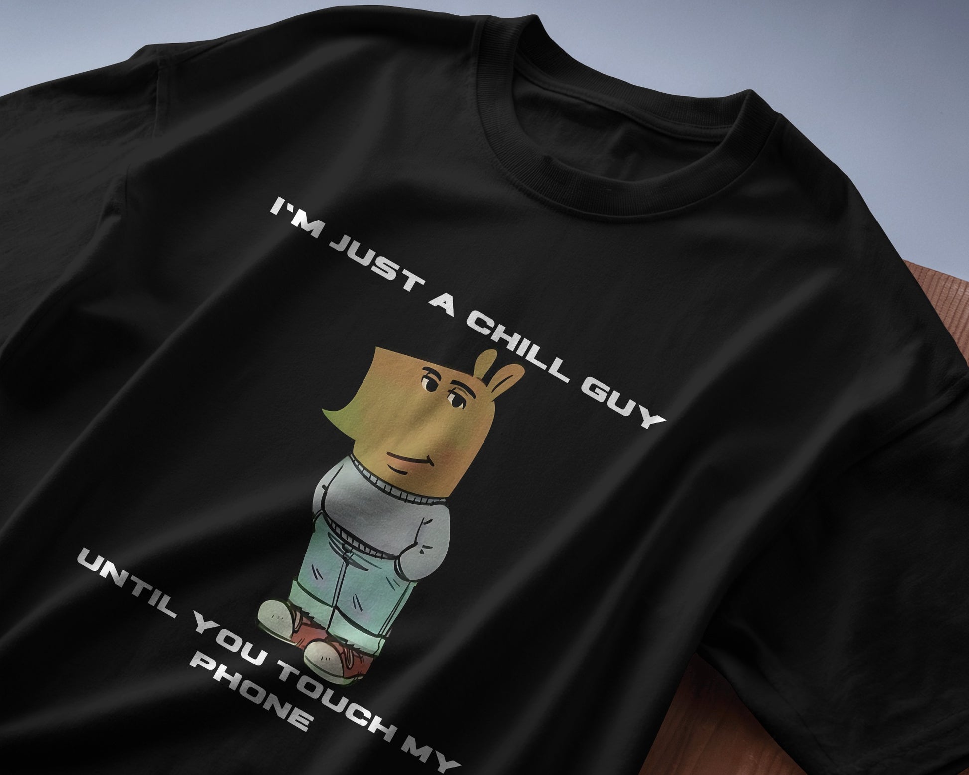 black "I’m Just a Chill Guy… Until You Touch My Phone" tshirt laying on the table
