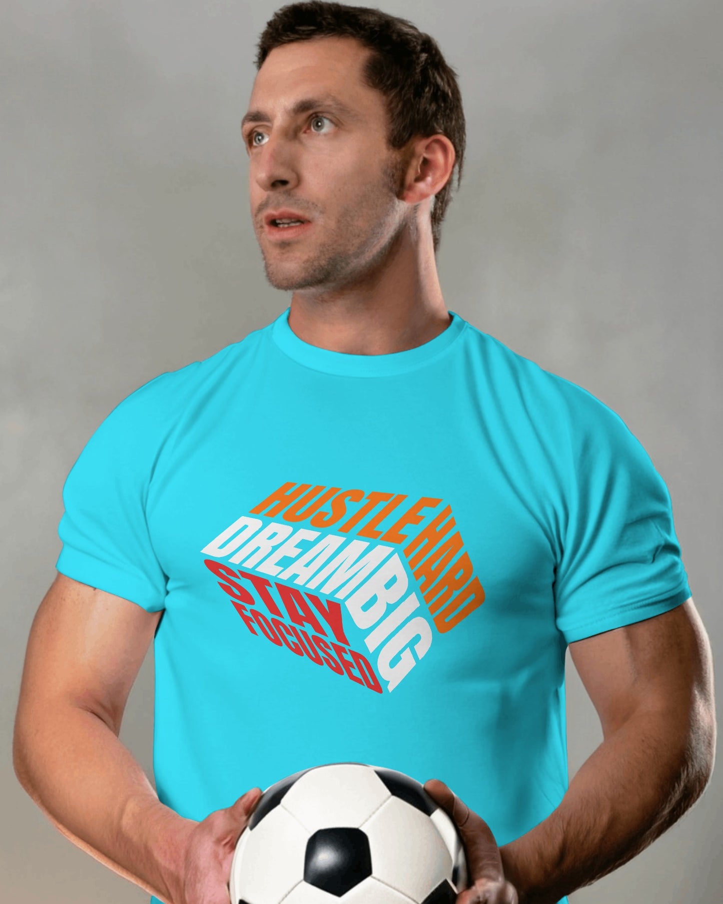 A male model standing with a football in his hands wearing 'Hustle Hard' tshirt in Sky Blue color