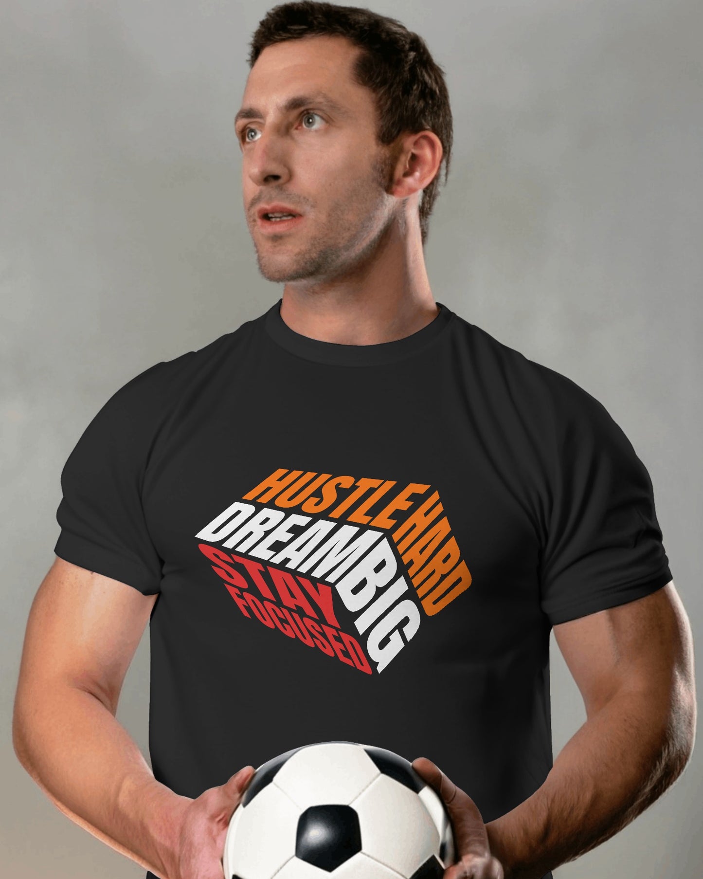 A male model standing with a football in his hands wearing 'Hustle Hard' tshirt in Black color