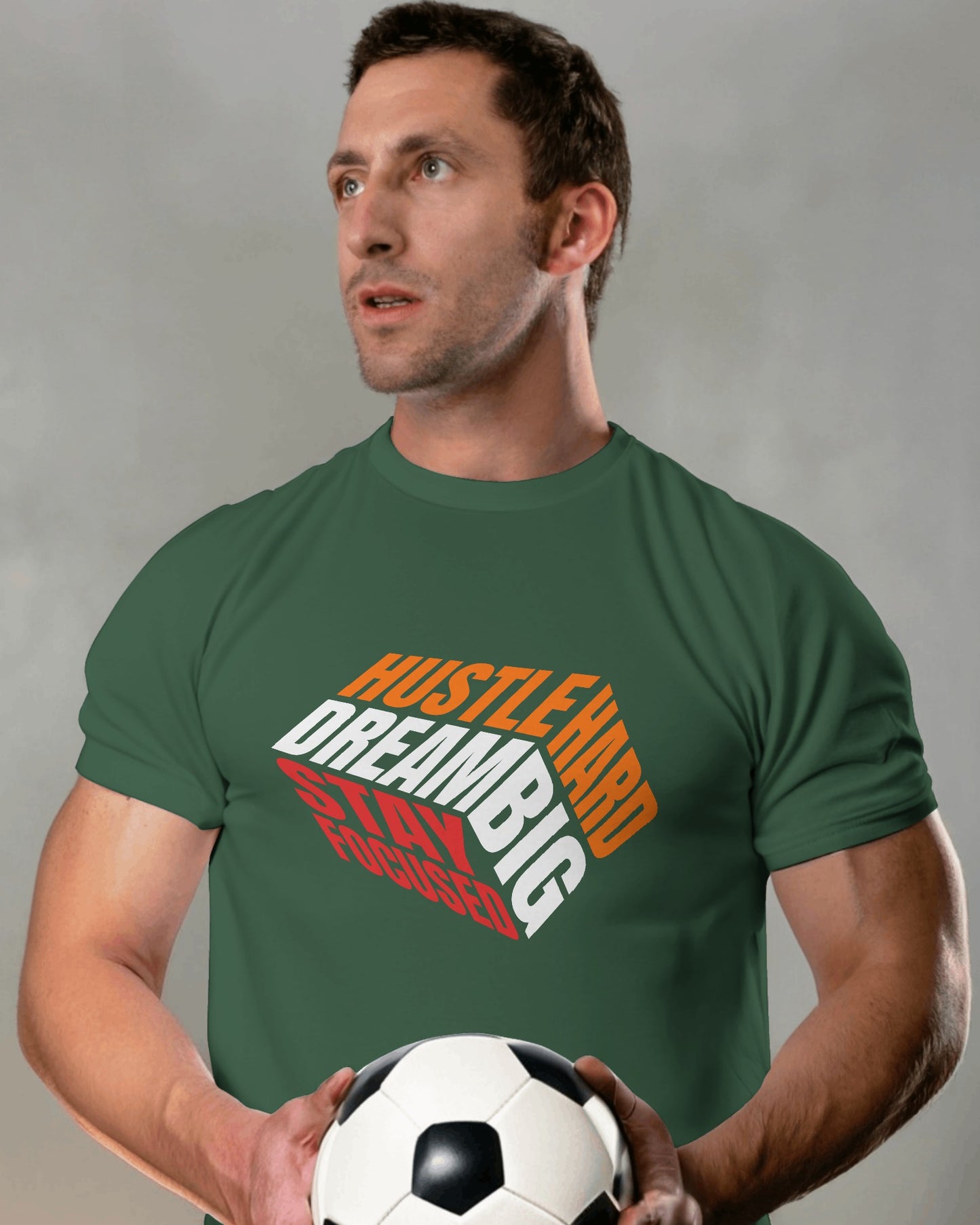 A male model standing with a football in his hands wearing 'Hustle Hard' tshirt in Bottle Green color