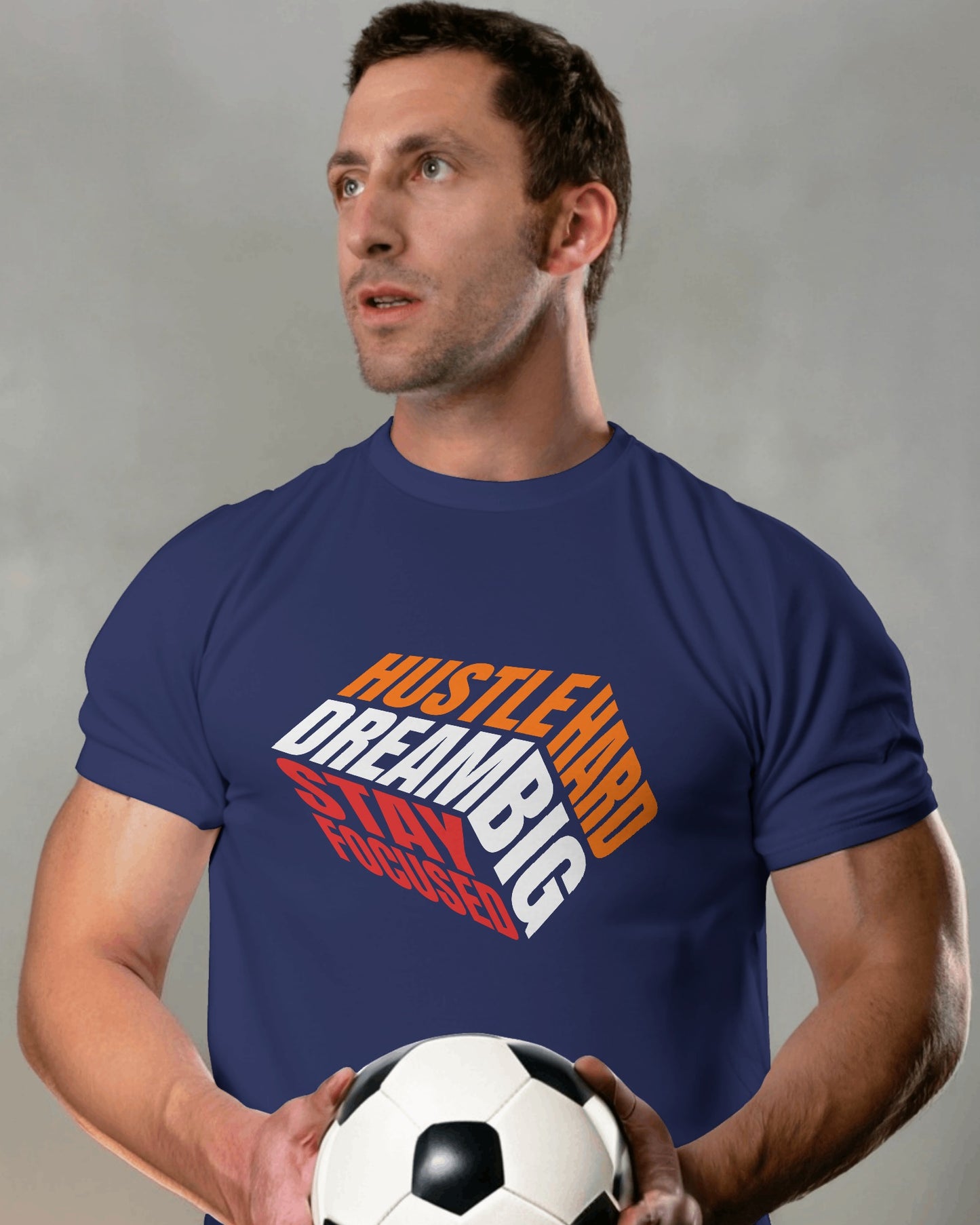 A male model standing with a football in his hands wearing 'Hustle Hard' tshirt in Navy Blue color