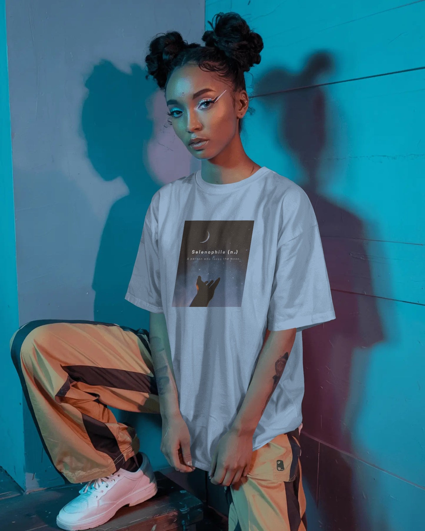 a female black model standing wearing an oversized baby blue Selenophile tshirt with a neon lit background