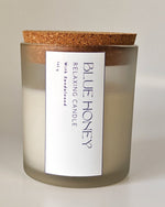 Frosted glass jar candle with a cork lid, labeled 'Blue Honey Relaxing Candle with Sandalwood'.