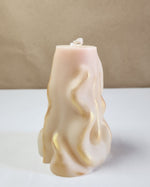 A 3D wave white soy wax pillar candle with gold accents, standing on a white surface.