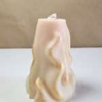 A 3D wave white soy wax pillar candle with gold accents, standing on a white surface.