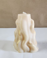 A 3D wave white soy wax pillar candle with gold glitter accents sits on a white surface.