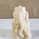 A 3D wave white soy wax pillar candle with gold glitter accents sits on a white surface.