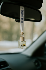 Reed oil car diffuser with natural fragrance hanging from a car's rearview mirror, featuring a wooden cap and a small flower.