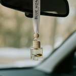 Reed oil car diffuser with natural fragrance hanging from a car's rearview mirror, featuring a wooden cap and a small flower.