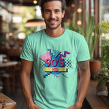 A smiling man wears a mint green '90s Kid' t-shirt in a lifestyle setting.