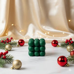 A green soy wax bubble candle is displayed on a marble surface with festive Christmas decorations.
