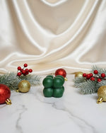 A green bubble soy wax candle sits on a marble surface surrounded by festive Christmas ornaments and pine branches.