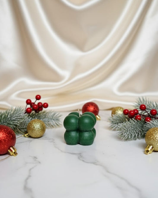 A green bubble soy wax candle sits on a marble surface surrounded by festive Christmas ornaments and pine branches.