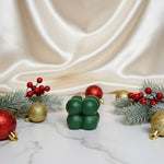 A green bubble soy wax candle sits on a marble surface surrounded by festive Christmas ornaments and pine branches.