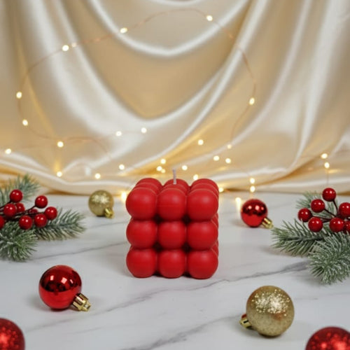 A red bubble candle sits on a marble surface surrounded by Christmas ornaments and greenery.