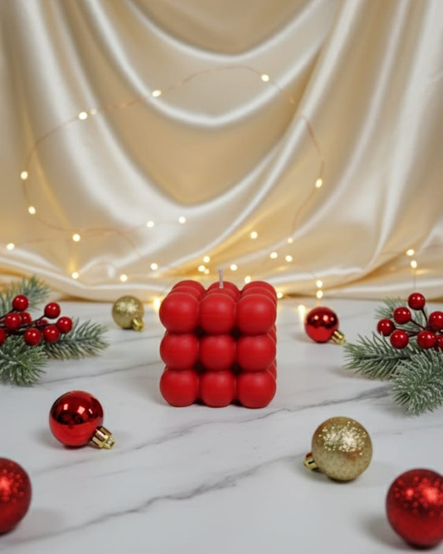 A red bubble candle sits on a marble surface surrounded by Christmas ornaments and greenery.