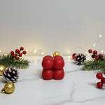 A red bubble soy wax candle with Christmas decorations like pine cones and berries on a marble surface.