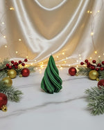 A green soy wax Christmas tree candle sits on a marble surface surrounded by festive decorations.