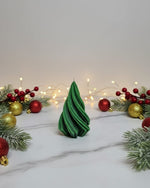 A green, twisted Christmas tree-shaped soy wax candle sits on a marble surface, surrounded by festive decorations.