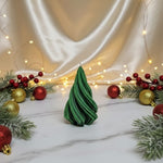A green soy wax Christmas tree candle sits on a marble surface surrounded by festive decorations.