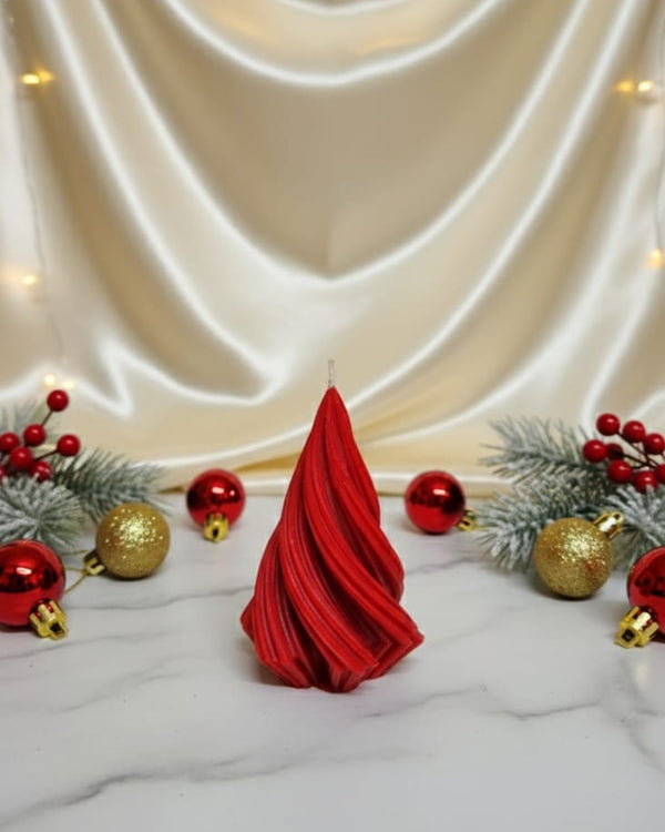 A red, twisted Christmas tree-shaped soy wax candle sits on a marble surface with festive decorations.