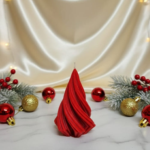 A red, twisted Christmas tree-shaped soy wax candle sits on a marble surface with festive decorations.