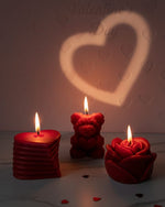Three red Valentine's Day sculpted candles: heart, teddy bear, and rose, casting a heart shadow.
