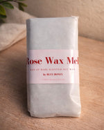 A bar of rose-scented soy wax melt, wrapped in white paper with a pink label.