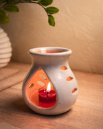 White ceramic heart-shaped aromatherapy diffuser with a lit red candle inside, on a wooden surface.