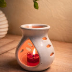White ceramic heart-shaped aromatherapy diffuser with a lit red candle inside, on a wooden surface.