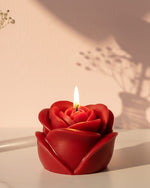 A red sculpted rose-shaped candle with a lit wick, perfect for romantic gifting and decor.