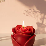 A red sculpted rose-shaped candle with a lit wick, perfect for romantic gifting and decor.
