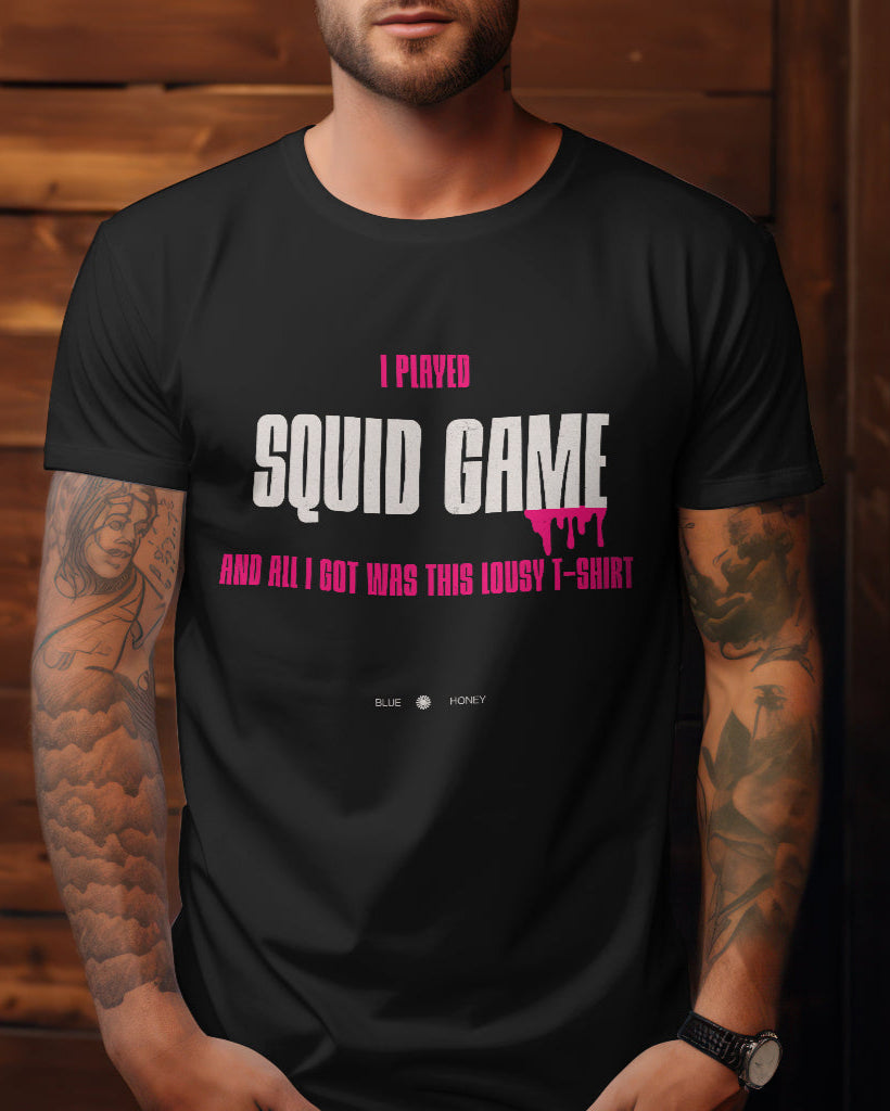 A male model with his hands in the pockets wearing a black t-shirt with the quote 'I Played Squid Game and All I Got Was This Lousy T-Shirt'