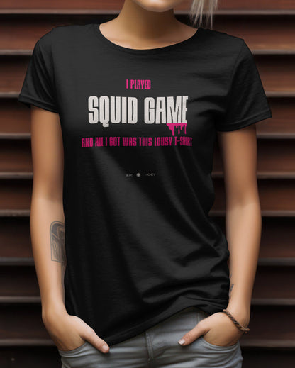 A female model with her hands in her pockets wearing a black t-shirt with the quote 'I Played Squid Game and All I Got Was This Lousy T-Shirt'