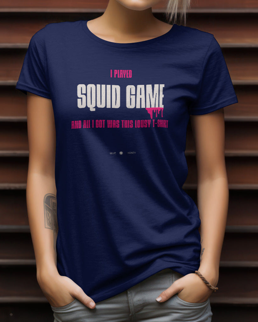 A female model with her hands in her pockets wearing a navy blue t-shirt with the quote 'I Played Squid Game and All I Got Was This Lousy T-Shirt'