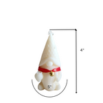 A white soy wax pillar candle shaped like a gnome with a red ribbon and bell, measuring 4 inches tall.