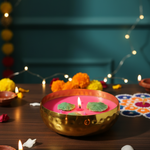 A hammered brass urli bowl filled with pink soy wax candle, decorated with lotus leaves and lit wick.