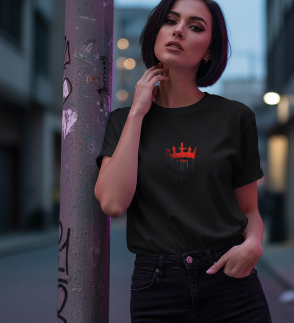 A woman wearing a black 'Wear the Crown. Own the Hype' t-shirt with a red crown graphic, leaning against a pole.