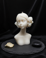 The Bloom Maiden Bust Candle, a white scented candle shaped like a woman's bust with floral accents.