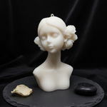 The Bloom Maiden Bust Candle, a white scented candle shaped like a woman's bust with floral accents.