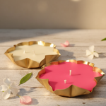Set of two lotus urli soy wax candles in brass bowls, one cream and one pink, with flowers and leaves.