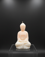 A light peach and cream colored meditating Buddha soy wax scented candle on a clear acrylic stand.